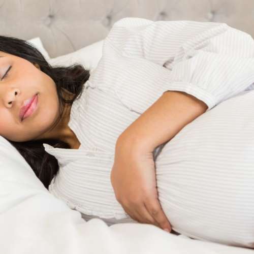 A pregnant woman sleeping on her side, holding her belly. 