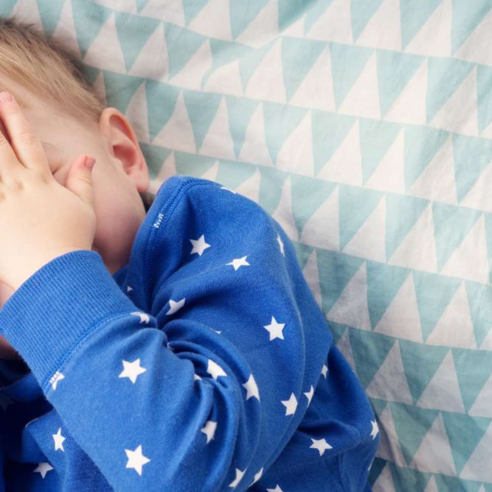 A one year old baby covering their face with their hands. 