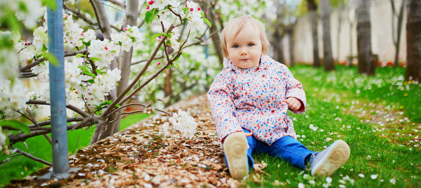 Baby sitting on grass near bloomed flowers