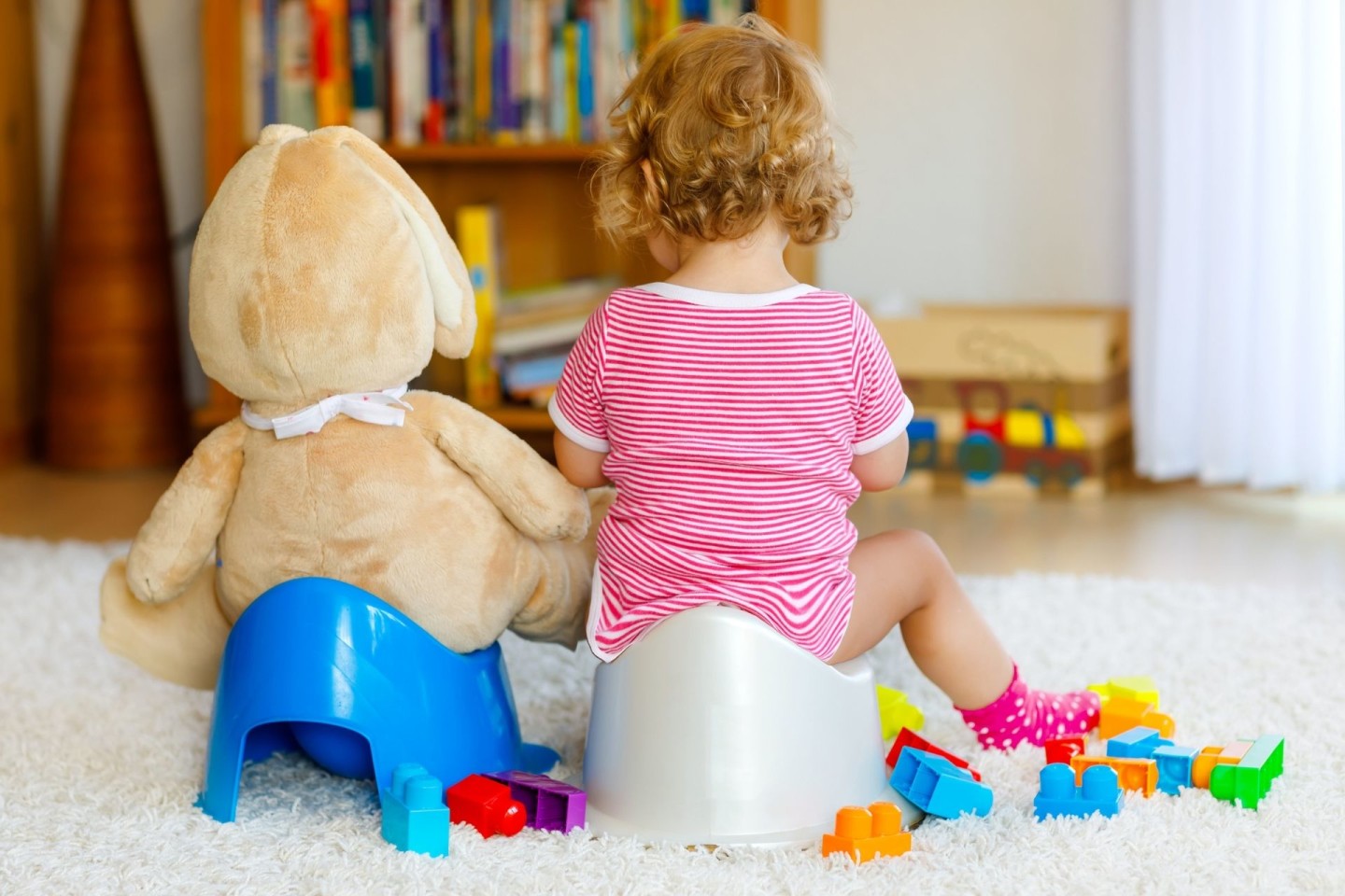 Toddler sitting on potty with stuffed animal sitting on play potty beside her