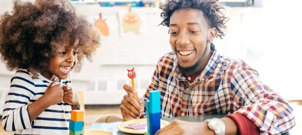 A child and their father are laughing and smiling while playing with blocks.