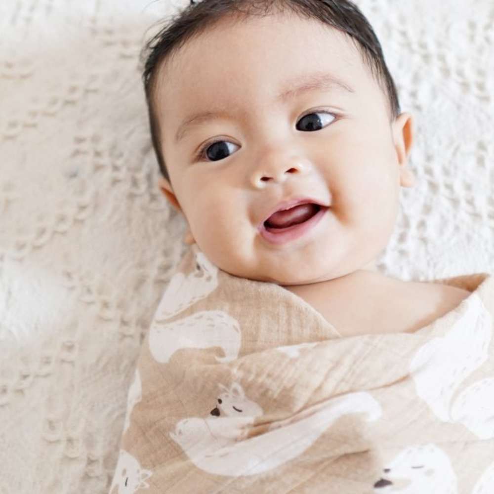 A baby is smiling while in a swaddle.