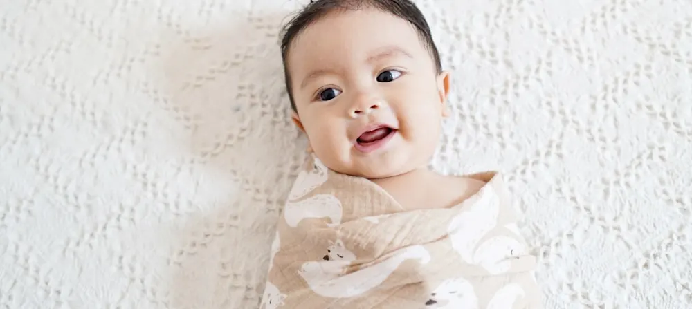 A baby is smiling while in a swaddle.