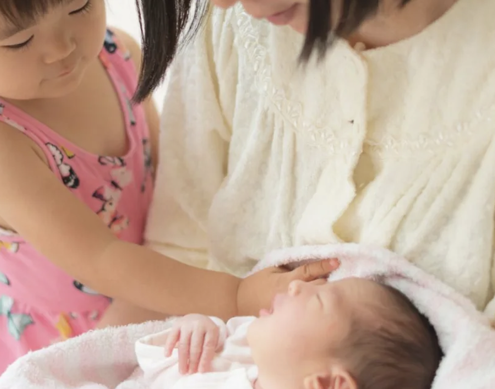 A little girl meeting her new baby sibling, while her mom holds the baby.
