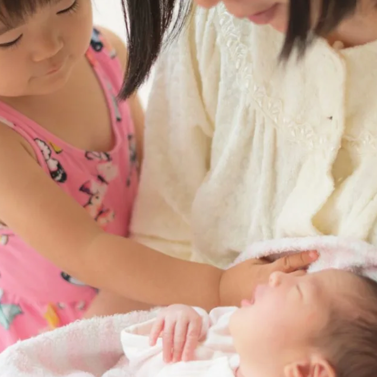 A little girl meeting her new baby sibling, while her mom holds the baby.