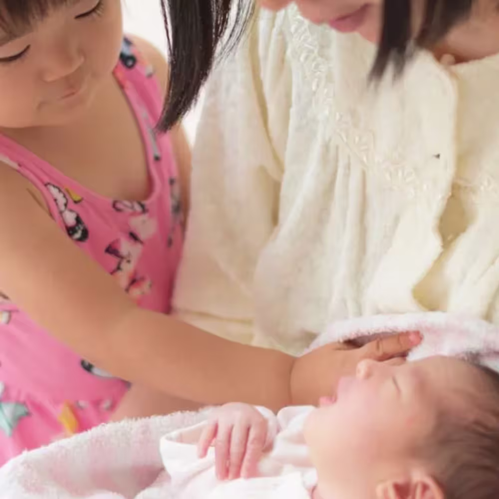 A little girl meeting her new baby sibling, while her mom holds the baby.