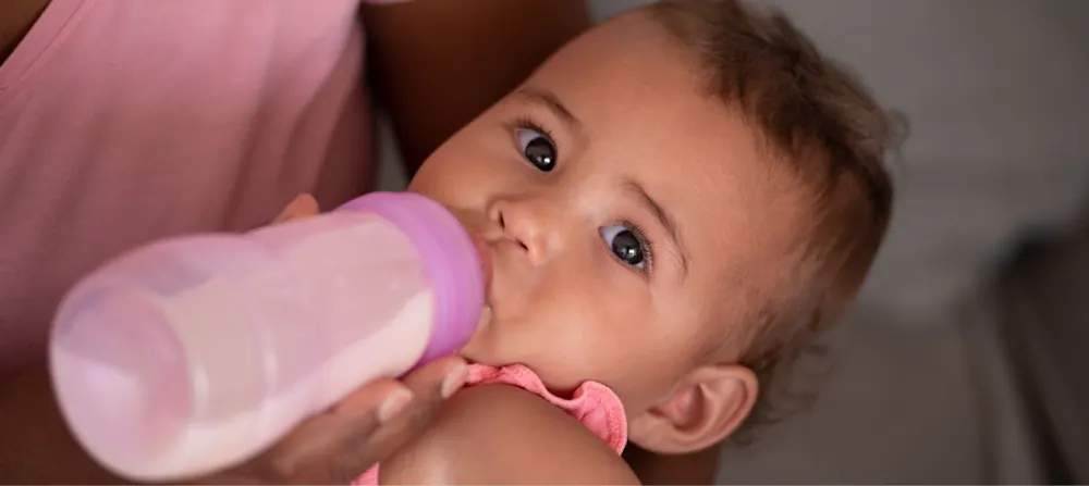 A caregiver feeding a child a formula bottle.