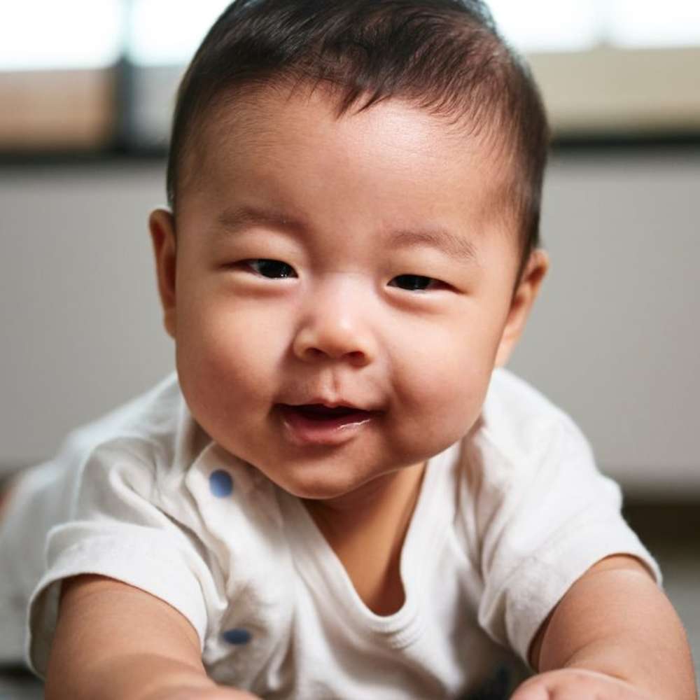 A baby smiling while lying down on their tummy. 