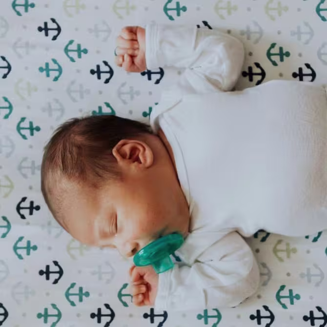 A baby sleeping on their back with a pacifier.
