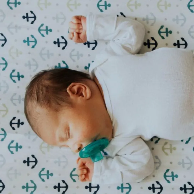 A baby sleeping on their back with a pacifier.