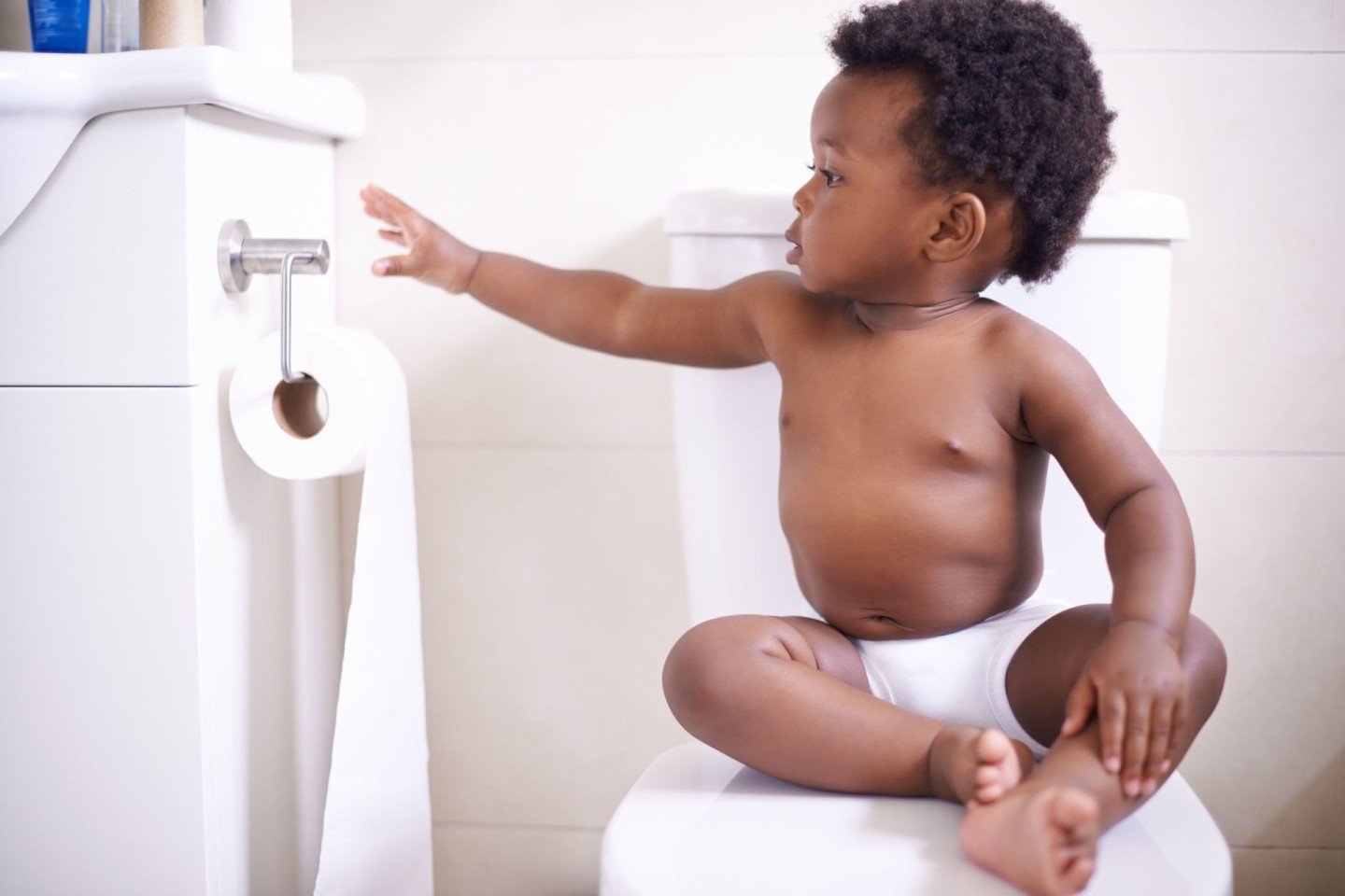 Toddler boy sitting on toilet and reaching for toilet paper