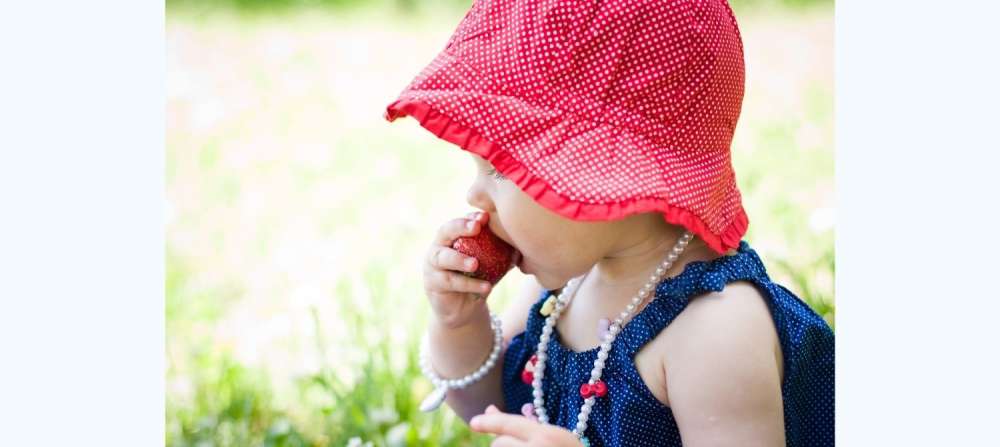 Baby sitting in grass eating strawberry