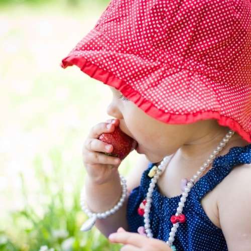 Baby sitting in grass eating strawberry