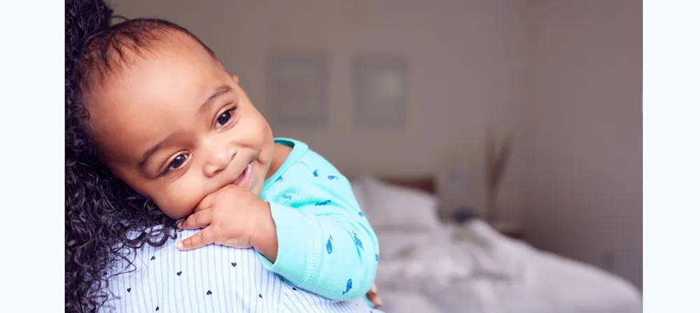 A caregiver is holding a baby, who is sucking on their thumb.