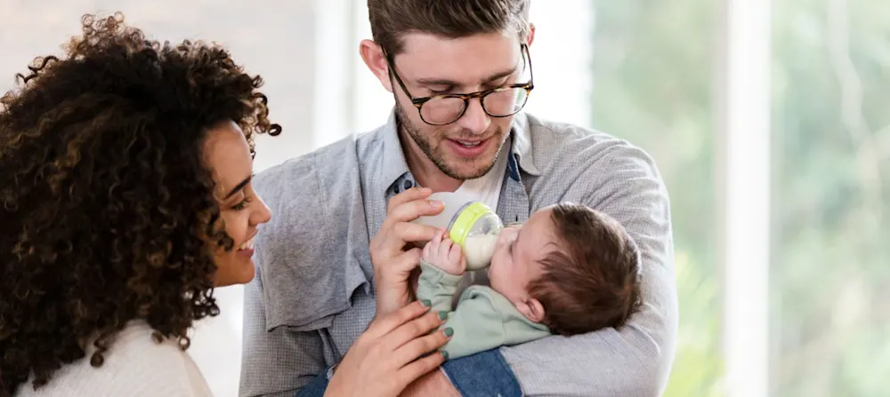 Two parents feeding their newborn baby.