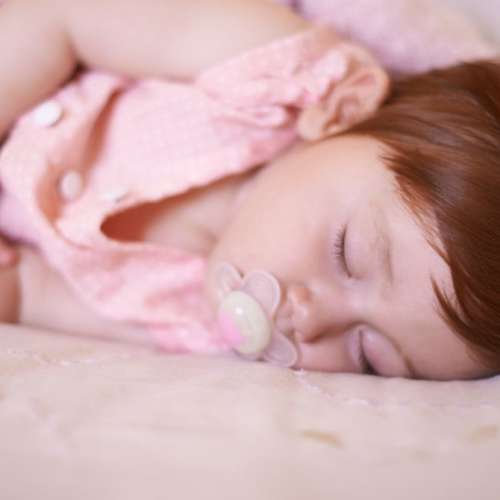 A child napping with a pacifier and blanket.