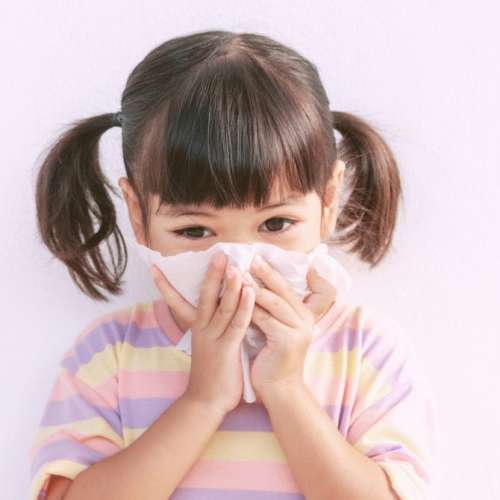 A girl blowing her nose in a tissue. 