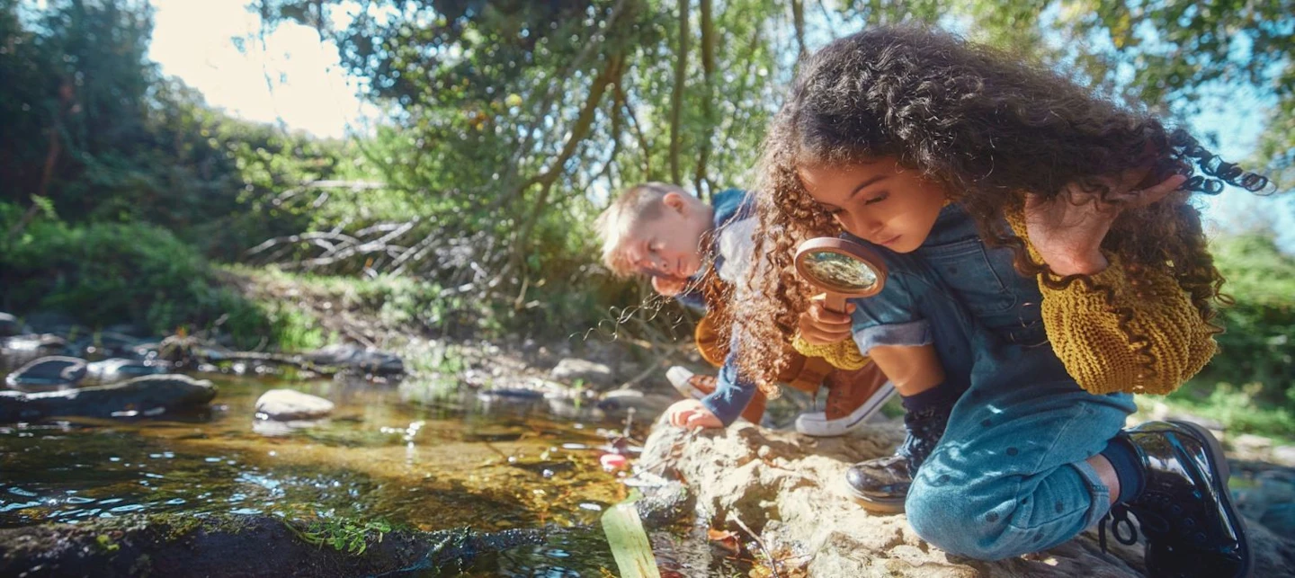 Two children outside looking at a creek. | Huckleberry