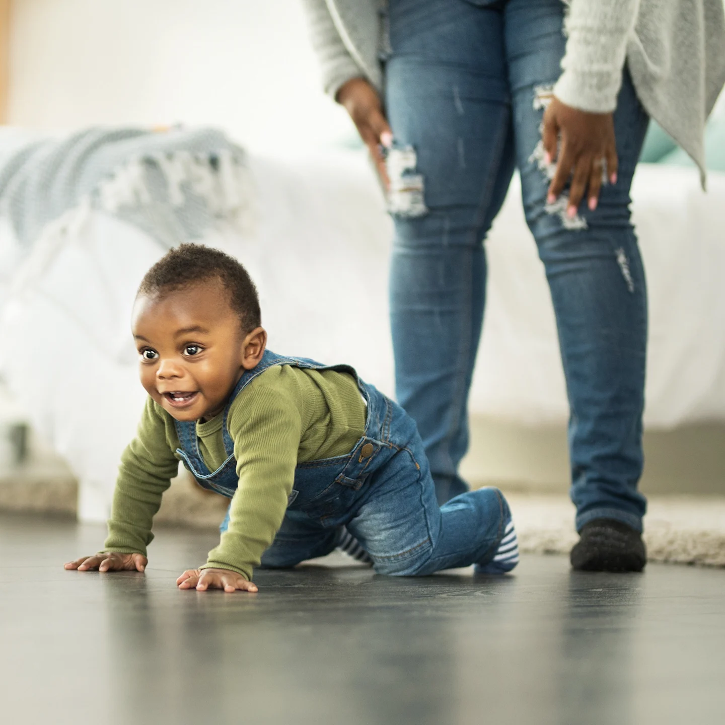 A baby crawling the classic crawl on the floor with mother looking on.