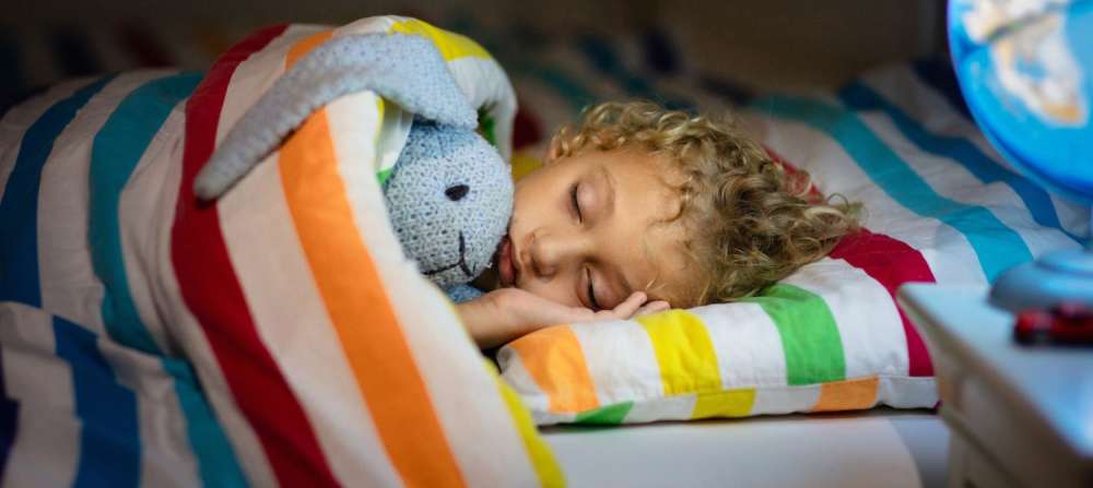 A photo of a young child sleeping with their stuffed animal, a rabbit. 