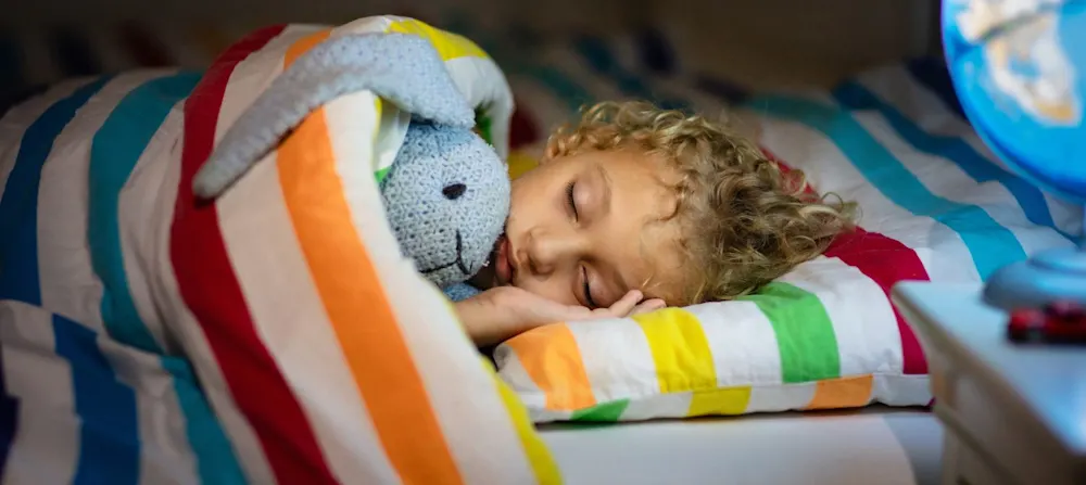 A photo of a young child sleeping with their stuffed animal, a rabbit.