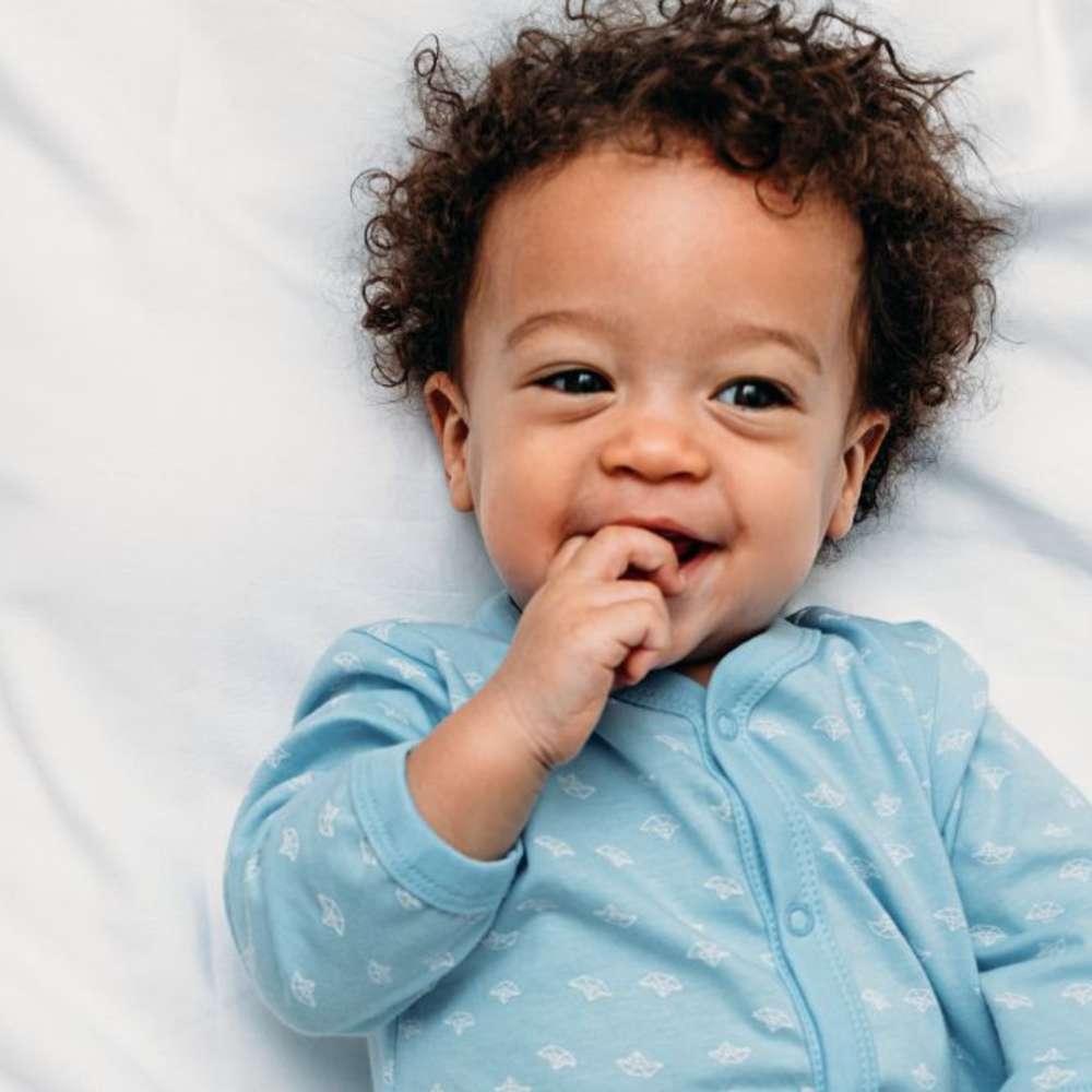 A smiling baby in a crib with a blue onesie on.