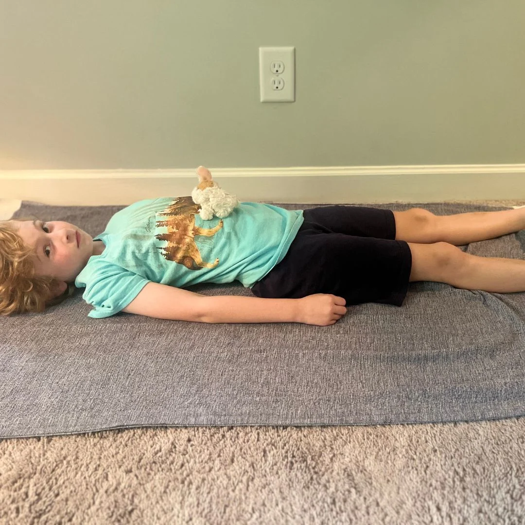A child doing a relaxation yoga pose with a stuffed animal on the belly.