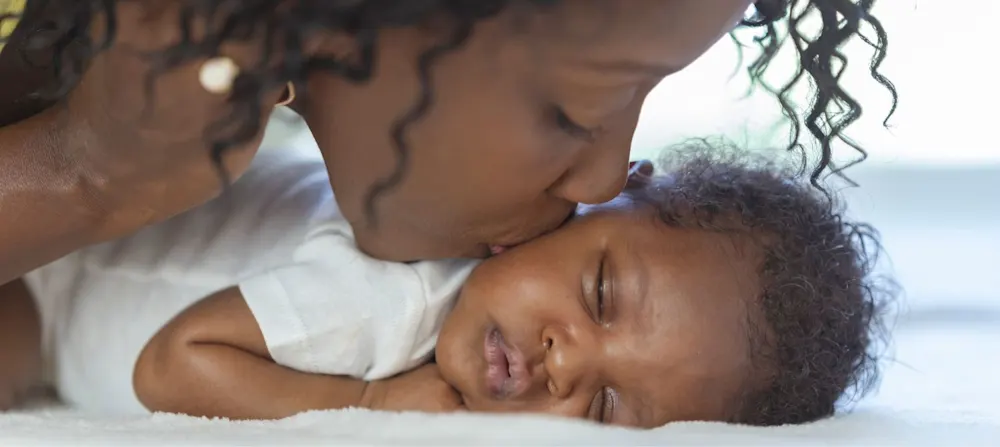 A mother kissing her sleeping baby.