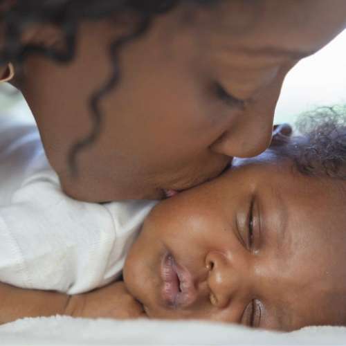 A mother kissing her sleeping baby.