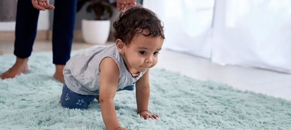 A baby crawling on a turquoise rug.
