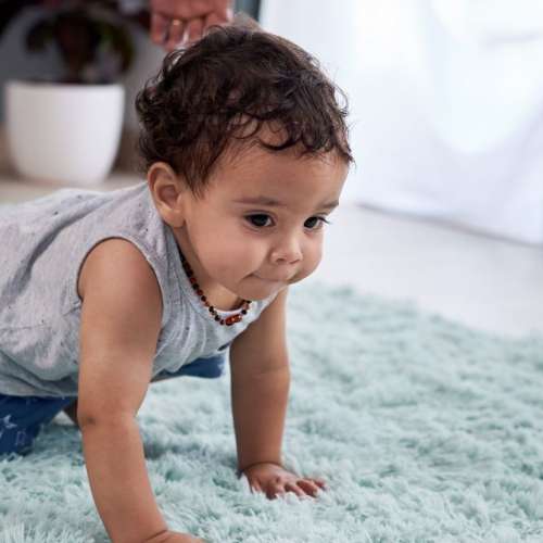 A baby crawling on a turquoise rug. 
