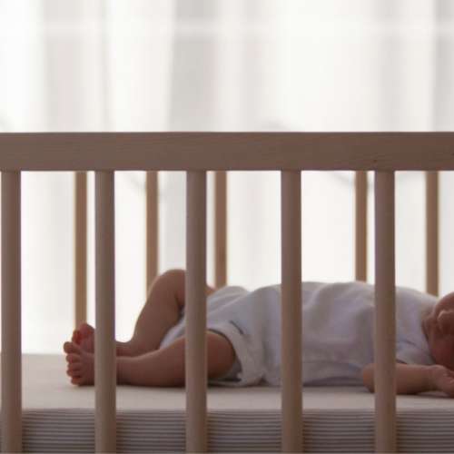 A baby sleeping in their crib, on their back.