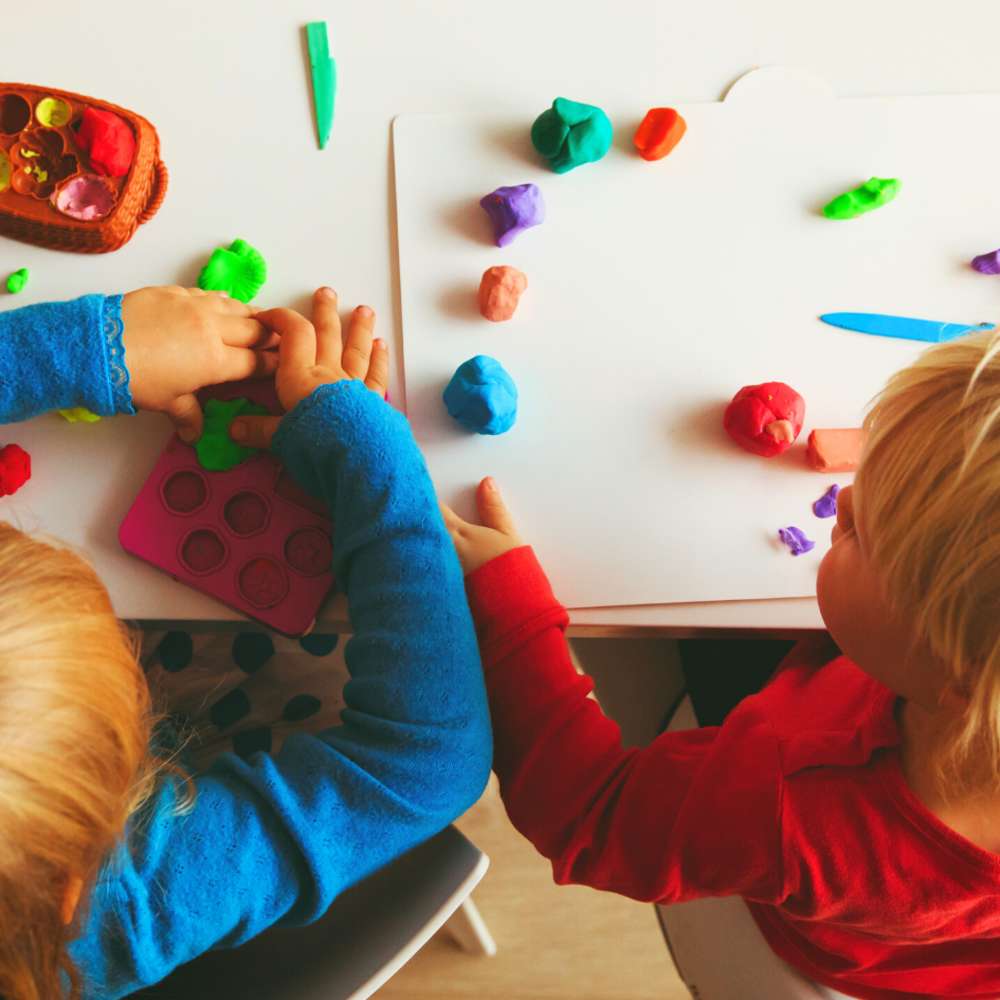 two kids playing on table with play doh