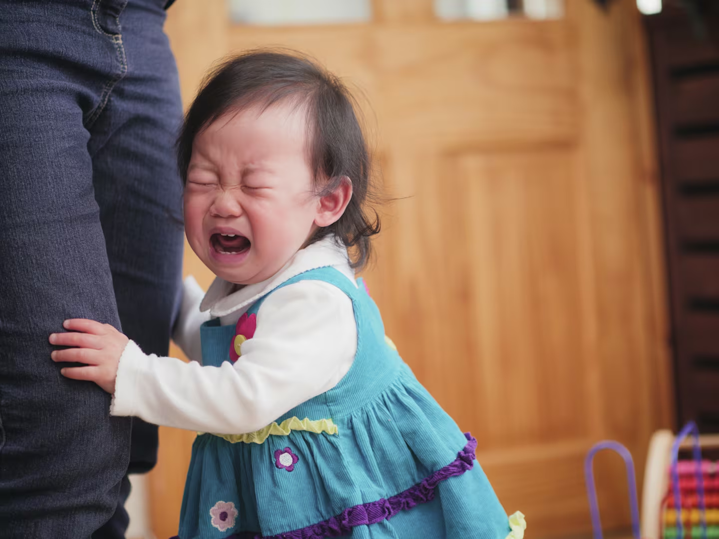 Separation anxiety in toddler: A fussing baby attached to mom at leg.