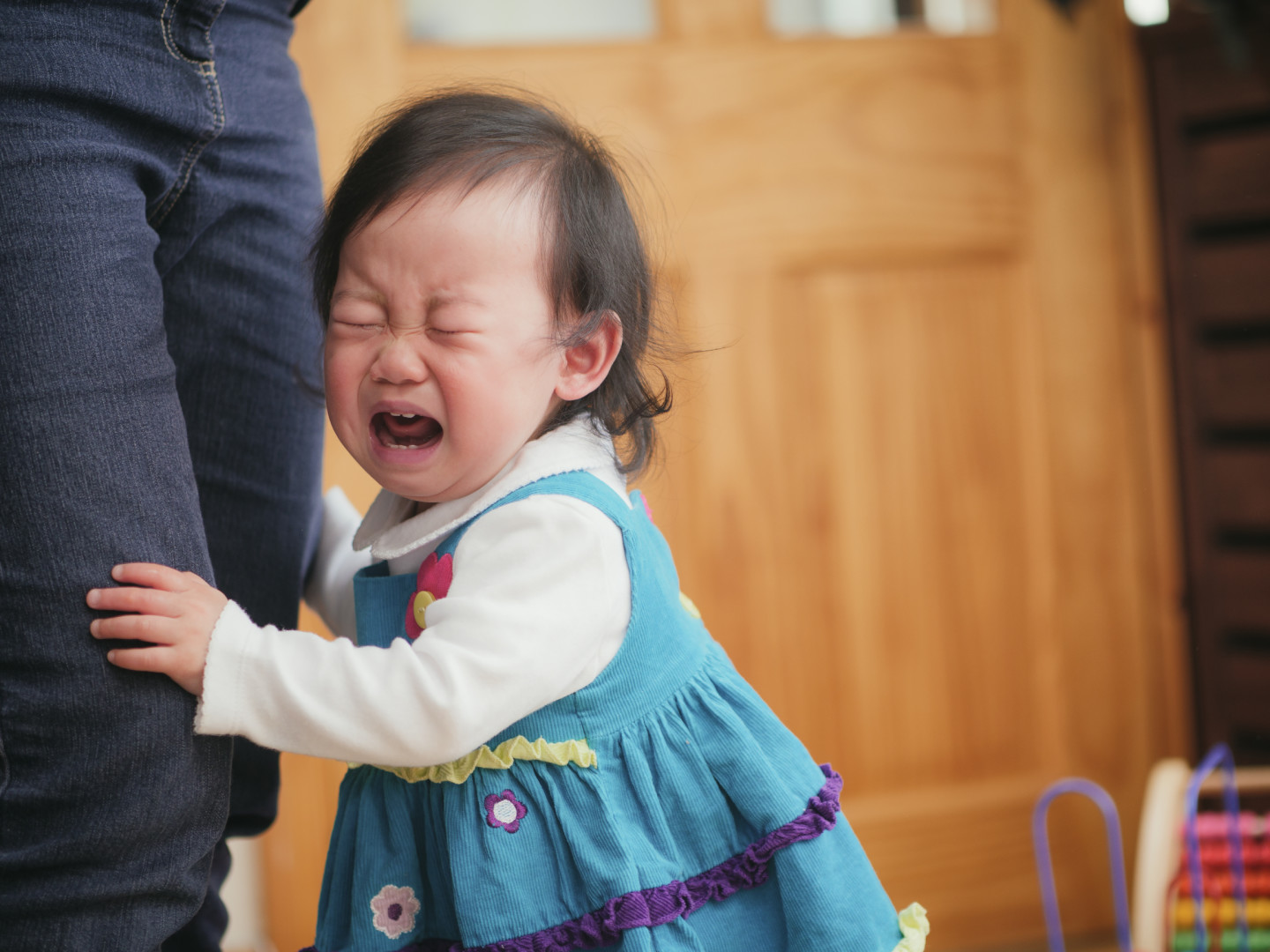 Separation anxiety in toddler: A fussing baby attached to mom at leg.