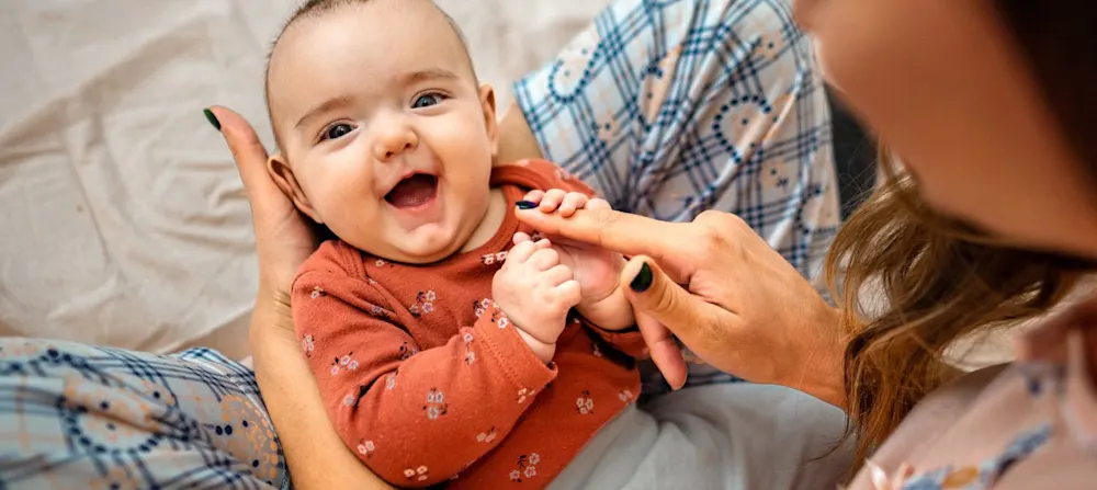 A baby smiling while their mom is holding them.