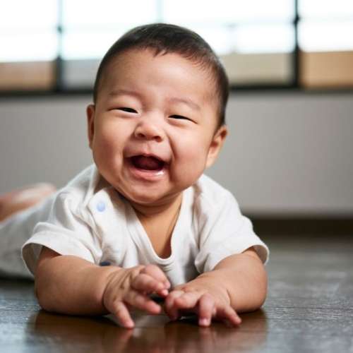 Smiling 8 month old baby on tummy on floor