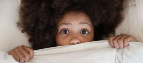 A child peeking over the bed covers.