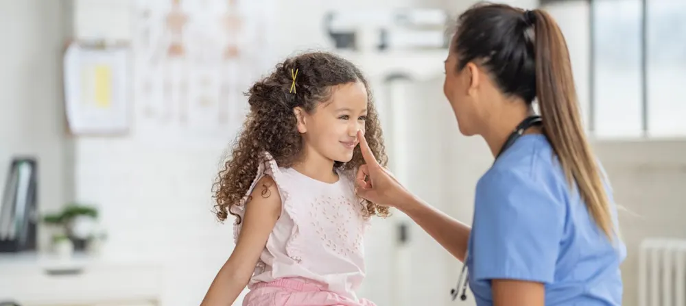 A child in the doctor's office, with a doctor looking at their nose.