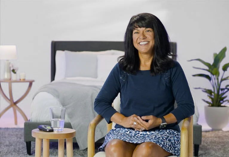 The image shows a woman sitting and smiling broadly at the camera.