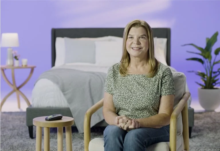 The image shows a woman sitting and smiling at the camera.