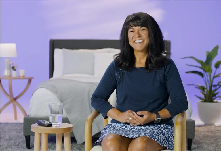 The image shows a woman sitting and smiling broadly at the camera.