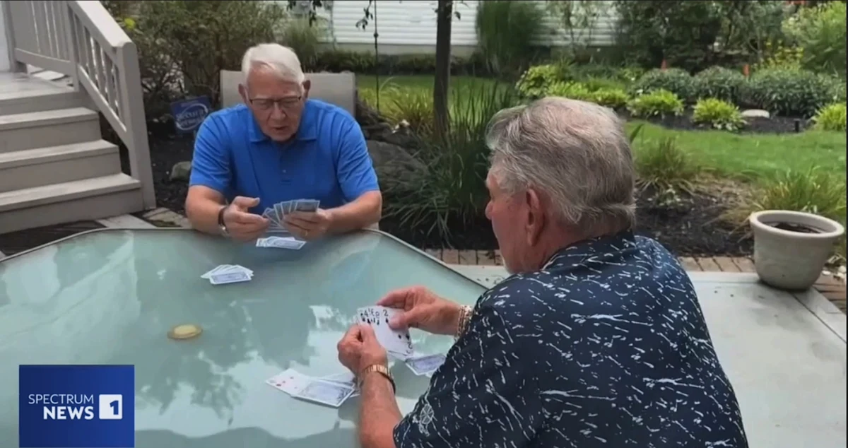 2 men playing cards outside on a patio table