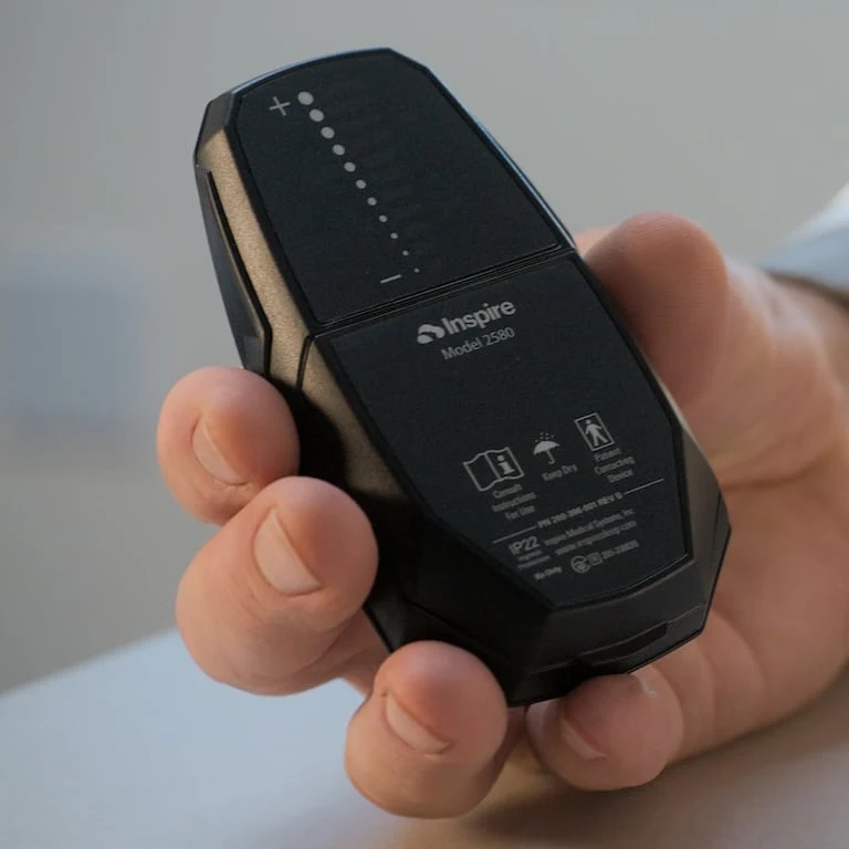 The image shows a close-up of a hand holding a Inspire Therapy device.