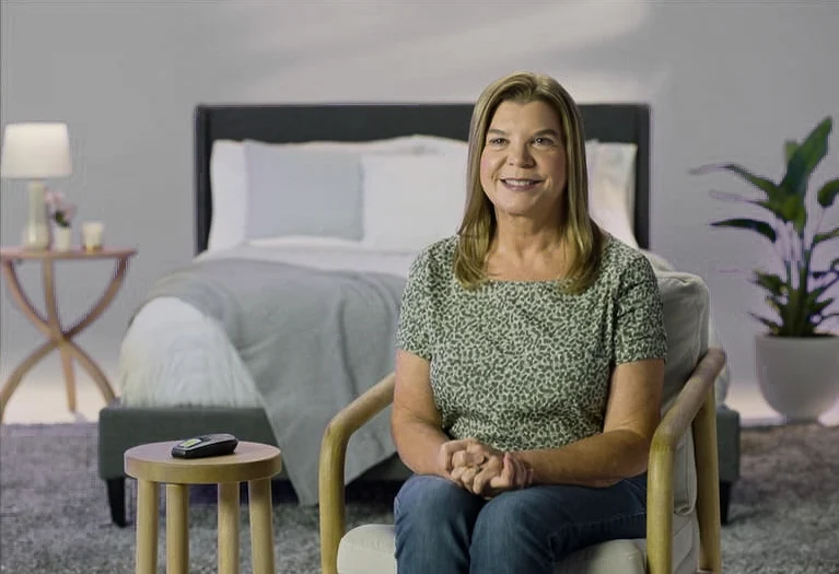 The image shows a woman sitting and smiling at the camera.