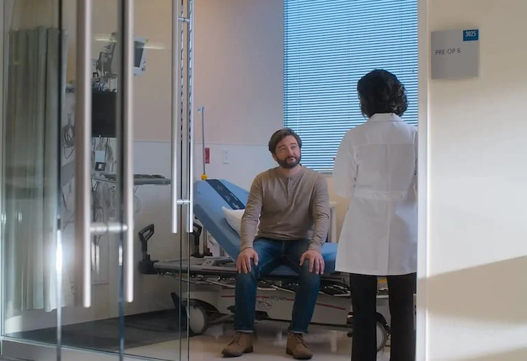 The image captures a moment inside a medical facility where a male patient, seated, is interacting with a healthcare professional standing opposite him.