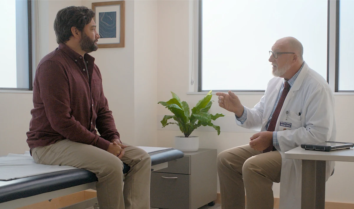 The image captures a moment between a male patient and a male healthcare provider in a medical office.