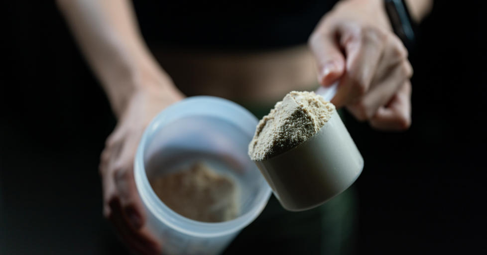 Close up of women with measuring scoop of whey protein and shaker bottle, preparing protein shake.