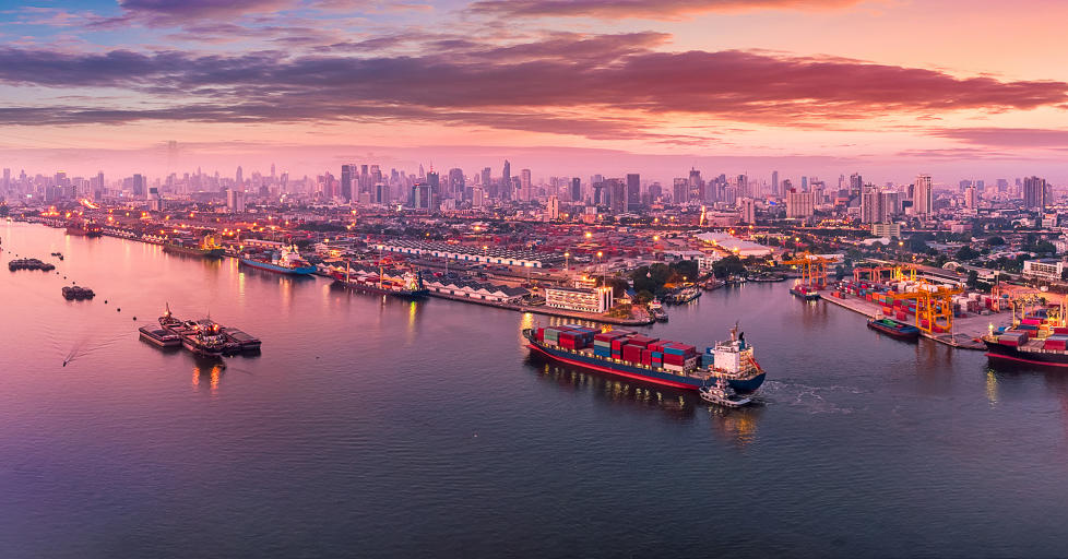 Aerial panoramic view of Logistics and transportation of Container Cargo ship and Cargo plane with working crane bridge in shipyard at sunrise