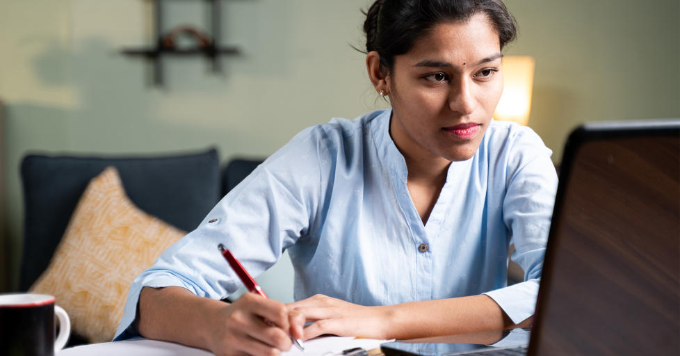 Young business woman writing down notes whilst attending an online training session in her home